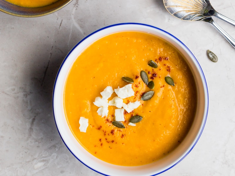 Creamy butternut squash soup garnished with pepitas and sage in a white bowl